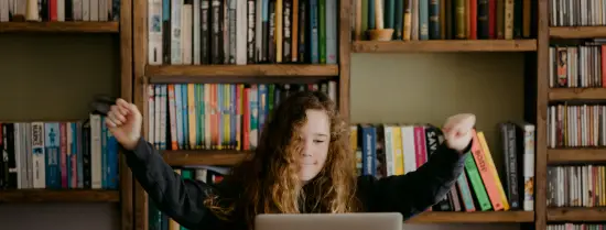 Meisje achter laptop steekt blij armen zijwaarts omhoog
