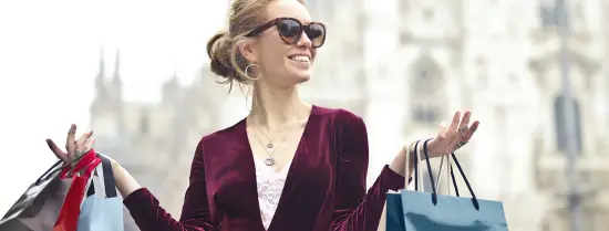 A women wearing fashionable sunglasses whilst holding up multiple high end shopping bags 
