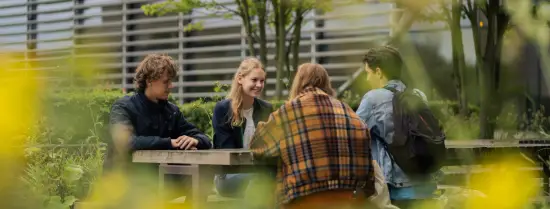 Vier studenten zitten aan een picknicktafel op campus Woudestein