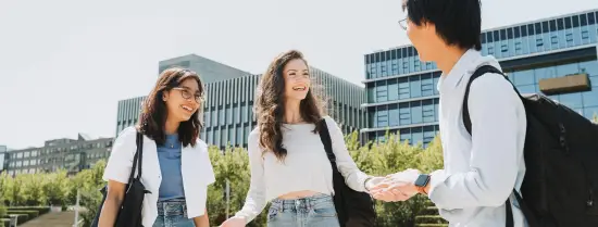 Drie studenten lachen op de campus in de zomer bij de vijver.