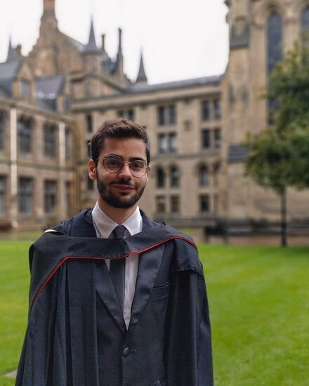 Man with short beard and glasses in front of beautiful old monumental building