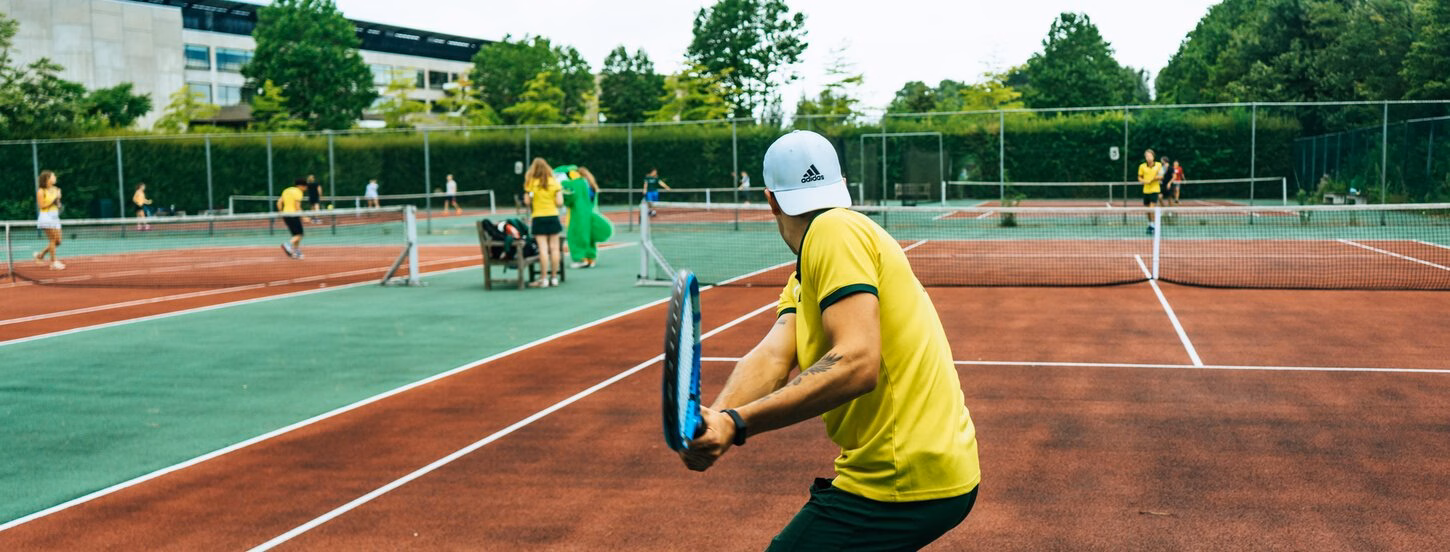 Person seen from behind in yellow T-shirt with tennis racket on tennis court.