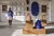 Art work sculptures on wooden steps and woman looking at art in frames on the wall
