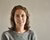 White woman with brown hair and a gray jumper against a beige background