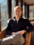 Young blond man with his legs crossed, sitting in a room with a lot windows
