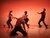 four dancers on stage. One on their knees in the fron. All tinted red. 