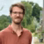Man in rust-colored shirt standing on a tree-lined path