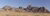 Panoramic view of reddish rocky hills under clear blue sky and a single industrial chimney smoking 