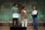 Photograph of a host interviewing two youths holding signs on stage with green grid backdrop