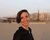 Alessia smiling with short dark hair on sandy beach with blurred harbor in background