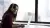 Vrouw met koptelefoon aan bureau met laptop bij een raam