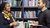 Two students standing in front of a shelf with books on urban development, holding open books and smiling while making eye contact