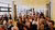 An audience sitting in a room with yellow walls, clapping