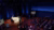A hall with several rows of seats and a white table in the front. People in the audience watch the conversation happening at the table.