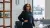 Alumni Asma poseert in haar kantoor naast haar werkbureau met laptop en blauw vloerkleed.
