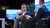 Men sitting with one leg on top of the other while making a gesture with his hands and the side profile of a man