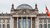 Front view of the German Reichstag building in Berlin, with the glass dome visible on top and the inscription ‘Dem Deutschen Volke’ on the facade, flanked by two German flags.