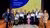 The award winners (or their delegates) holding their Awards on stage along with the hosts of the Awards ceremony