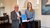 Man in blazer and woman holding blue certificate in conference room, both smiling