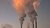 Photograph of industrial smokestacks emitting orange-tinged smoke into the sky
