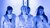 Four women wearing silver vests under blue lighting stand before metal truss