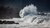 Large wave crashing against rocky shore under dark sky
