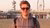 Young man in sunglasses and hoodie on beach at dusk with Ferris wheel and pier