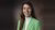 Smiling woman in a green blazer and white turtleneck against a brown backdrop.