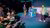 Two presenters on a colored-lit conference stage speaking to photographers crouched front