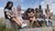 Photograph of eight diverse teens seated on outdoor stone bleachers, each focused on a smartphone