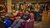 Man lounging on a red armchair, flashing peace sign in busy indoor furniture showroom