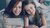 Mother and daughter lying on bed, smiling while taking a smartphone selfie.