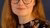Red-haired woman in glasses and a floral blouse smiles against dark blue background