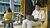 Photo of man in light suit using laptop in yellow lounge chair, woman reading behind him