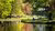 A pond in which green and orange trees are reflected, with people lounging on the grassy bank.