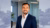 Smiling bearded man in navy blazer and white shirt standing in modern office