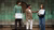 Photograph of a host interviewing two youths holding signs on stage with green grid backdrop
