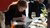 Photograph of a woman writing at a café table with documents, wine glasses and colleagues.