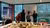 Four people sketching on a glass board above a table with a scale city model in an office