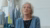 Senior woman with white hair and blue cardigan sitting in a sewing studio