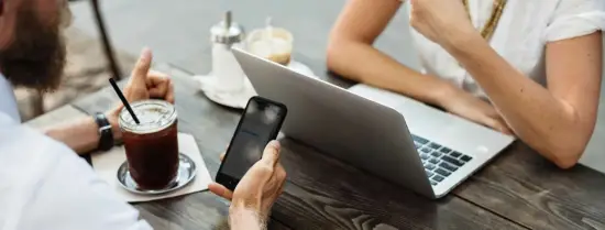 2 people sitting at a table with a laptop, smartphone and coffee