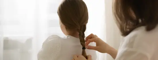 A person braiding the hair of a child