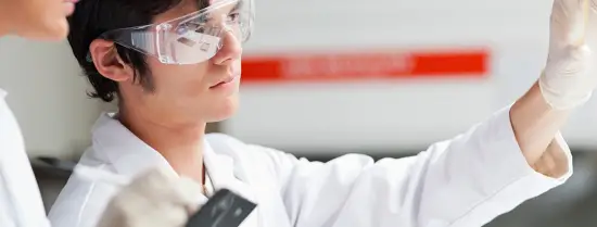 Person dressed in a lab coat and safety glasses holding a tube
