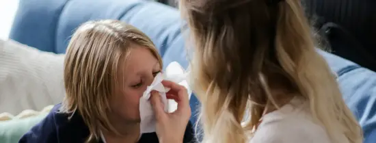 kid blowing his nose whilst his mother is holding the tissue
