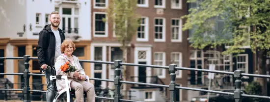 zorgverlener duwt vrouw in roelstoel vooruit in Amsterdam