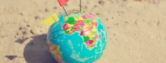 miniature globe laying on the beath with flags pinned into it