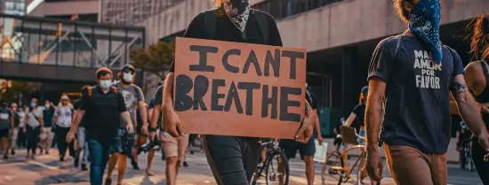Person walking on the street with a cardboard sign with the text 'I can't breathe'